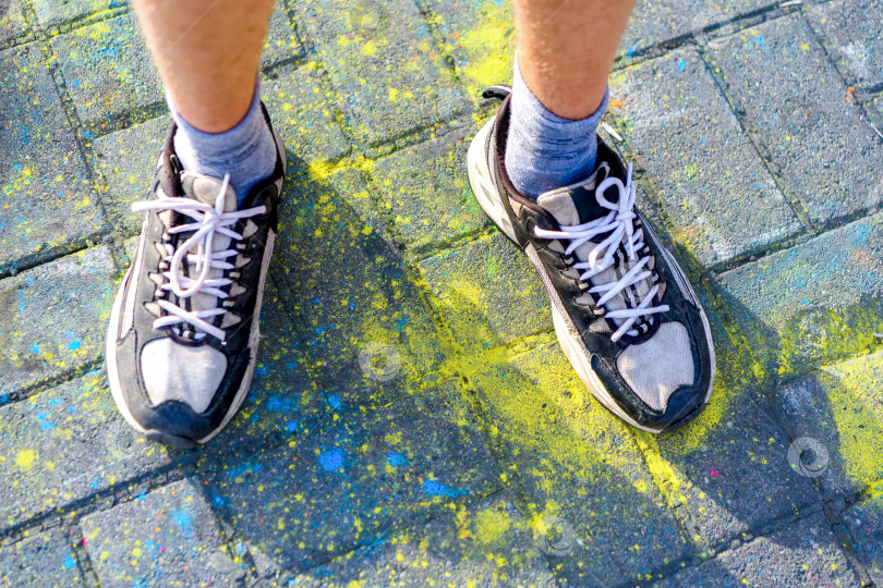 Скачать Мужские ноги в кроссовках selective focus стоят на асфальте, раскрашенном в цвета Холи. Концепция празднования Холи. фотосток Ozero