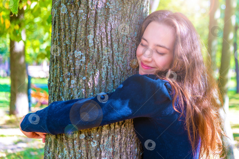 Скачать Молодая красивая девушка с любовью обнимает большое дерево в лесу на солнышке во время прогулки. Концепция сохранения леса, прекращения вырубки лесов. Снимок сделан с подсветкой и солнечными бликами. фотосток Ozero