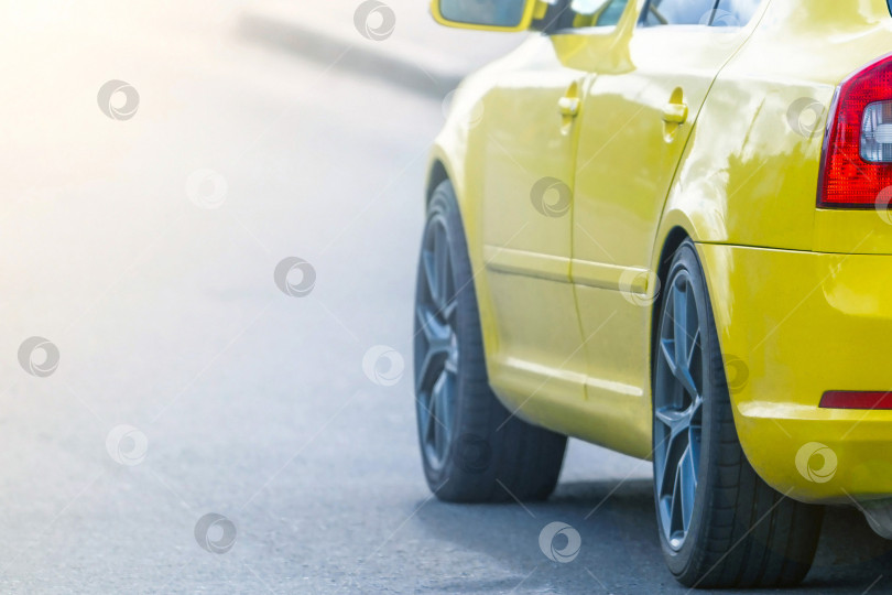 Скачать Задняя часть желтого современного спортивного автомобиля в селективном фокусе на закате во время движения по дороге. Снимок сделан с подсветкой и солнечными бликами. фотосток Ozero