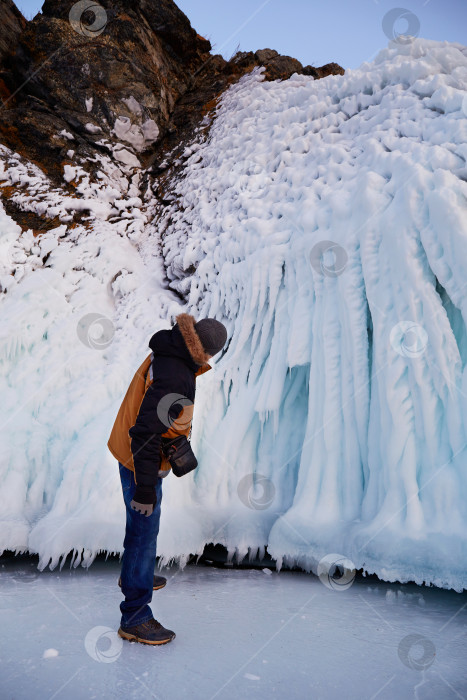Скачать Мужчина путешествует по замерзшему озеру Байкал. Турист смотрит на статуи или сосульки на скалах острова фотосток Ozero