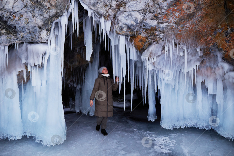 Скачать Женщина любуется огромными сосульками в ледяной пещере. Зимнее путешествие по замерзшему озеру Байкал. фотосток Ozero