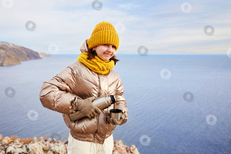 Скачать Молодая девушка-путешественница наливает горячий чай в кружку из термоса на природе. фотосток Ozero