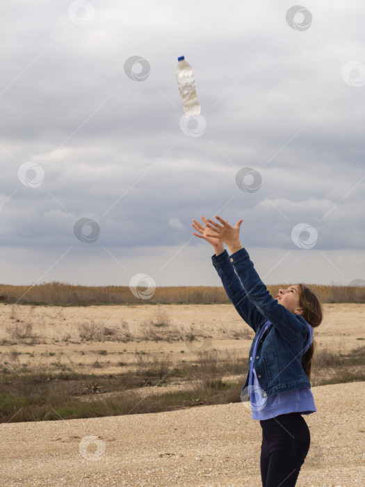 Скачать Девушка с поднятыми руками ловит бутылку с жидкостью на фоне пустынного пейзажа. фотосток Ozero