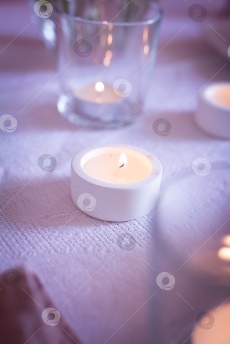 Скачать Горящая свеча в маленьком гипсовом подсвечнике на столе в окружении свечей в бокалах, выборочный фокус фотосток Ozero