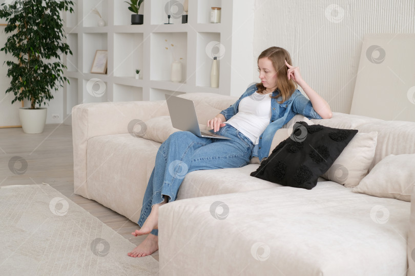 Скачать Милая красивая дама работает за ноутбуком, сидя дома на диване. концепция технологичной женщины для альтернативного офисного фрилансера. Удаленный домашний офис фотосток Ozero