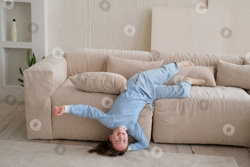 Скачать Счастливая школьница веселится, прыгает и переворачивается вверх тормашками на диване у себя дома. Время расслабиться. пространство для копирования. фотосток Ozero