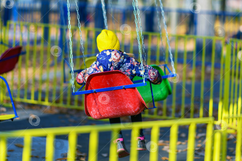 Скачать Маленькая девочка катается на качелях, карусели в парке развлечений.Прогулки с ребенком и детские развлечения. фотосток Ozero