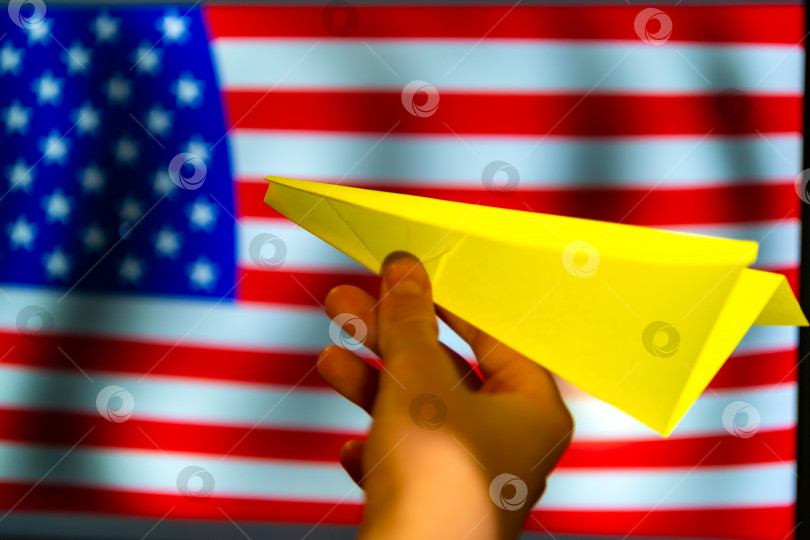 Скачать Расфокусированный вид бумажного самолетика на фоне флага США. Пространство для копирования. Концепция туристических рейсов в Америку. фотосток Ozero
