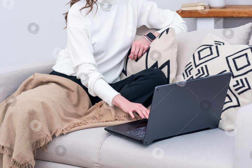 Скачать женщина, сидящая на диване в помещении и работающая с ноутбуком фотосток Ozero