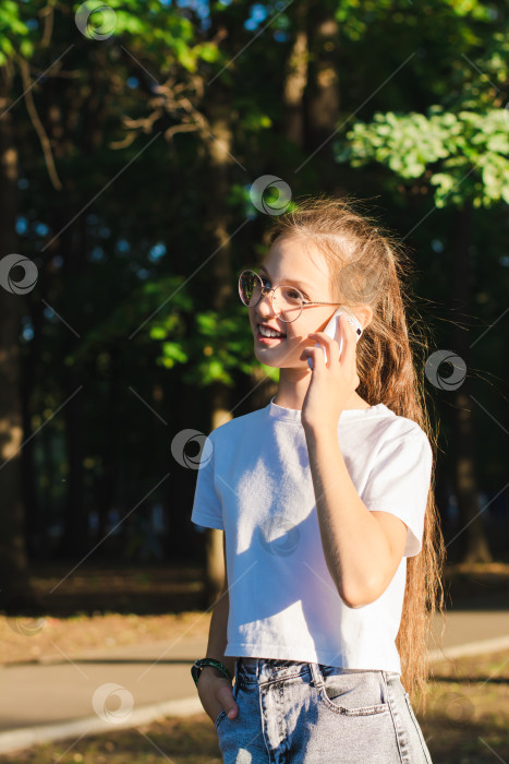 Скачать Девушка в очках радостно разговаривает по кнопочному телефону среди деревьев вертикальный вид фотосток Ozero