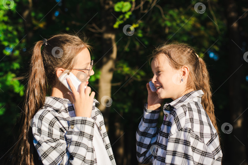 Скачать Две веселые девушки разговаривают по мобильным телефонам в солнечном летнем парке фотосток Ozero