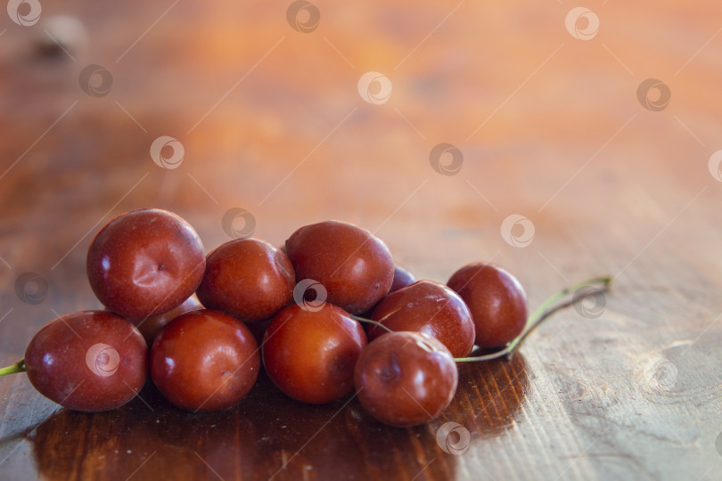 Скачать Спелые сочные ягоды унаби (зизифус) крупным планом на деревянной поверхности. Блестящий оранжево-красный фруктовый мармелад фотосток Ozero