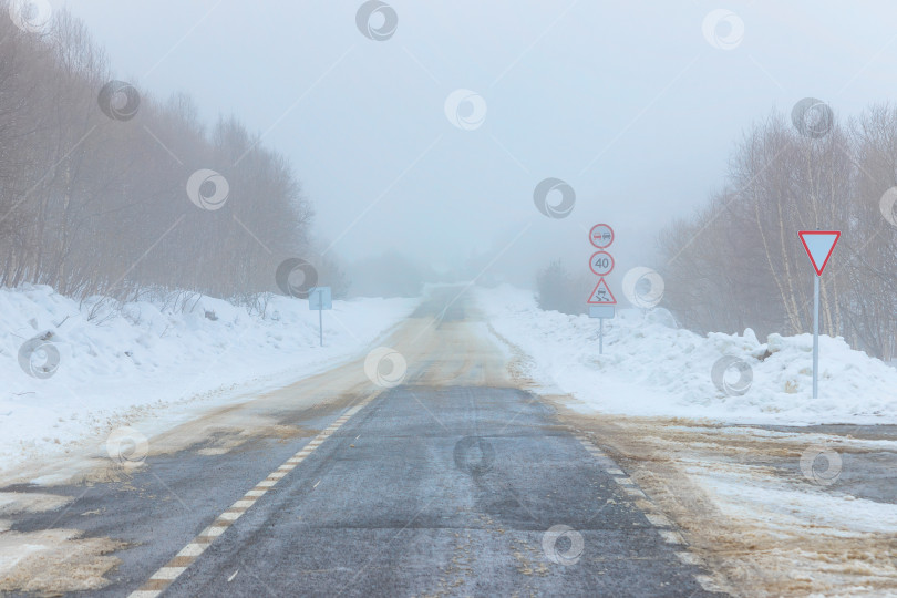 Скачать Пустая заснеженная дорога. Дорожные знаки, туман. Зимний пейзаж фотосток Ozero
