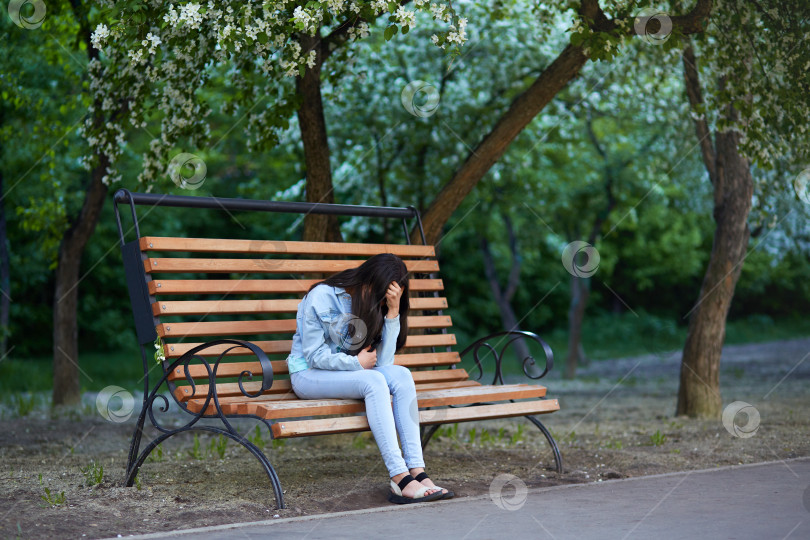 Скачать Расстроенная грустная девочка-подросток сидит на скамейке в парке, держась за голову и закрыв лицо руками фотосток Ozero