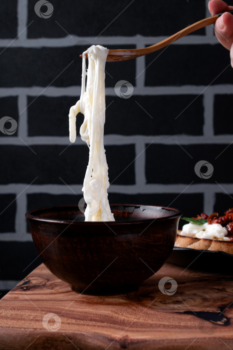 Скачать Сыр Страччателла нанизывается на вилку из миски со сливками. фотосток Ozero
