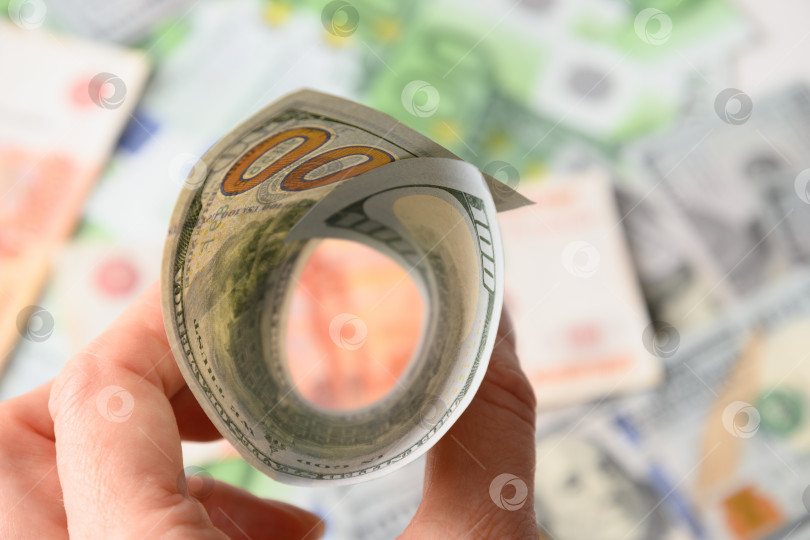 Скачать 100-долларовые купюры похожи на воронку в руке на фоне европейской валюты. фотосток Ozero