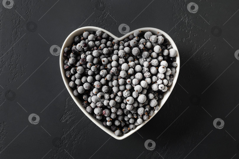Скачать Замороженная черная смородина в тарелке в форме сердца на черном фоне. Вид сверху. фотосток Ozero