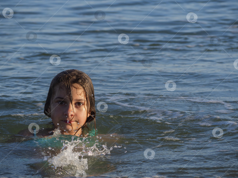 Скачать Красивая девушка купается в море под лучами заходящего солнца. Девочка-подросток наслаждается теплой морской водой.  Реальная жизнь, место для текста. фотосток Ozero