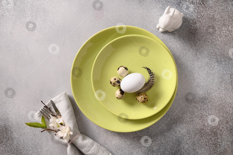 Скачать Пасхальная праздничная сервировка стола с серой тарелкой, весенними цветами и зелеными разноцветными яйцами. фотосток Ozero