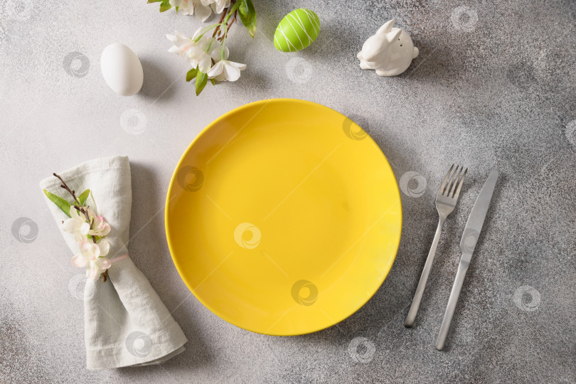 Скачать Пасхальная праздничная сервировка стола с желтой тарелкой, весенними цветами и зелеными разноцветными яйцами. фотосток Ozero