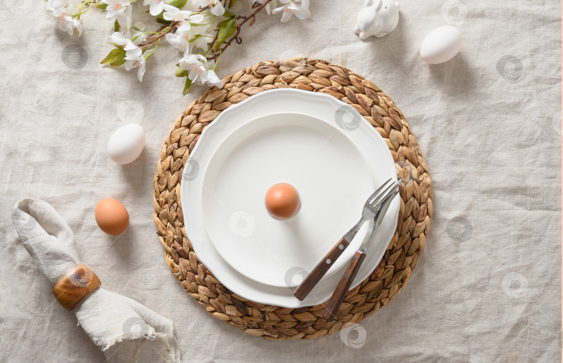 Скачать Праздничная сервировка стола на весеннюю Пасху с органическим коричневым яйцом, белым кроликом и цветущими цветами. фотосток Ozero