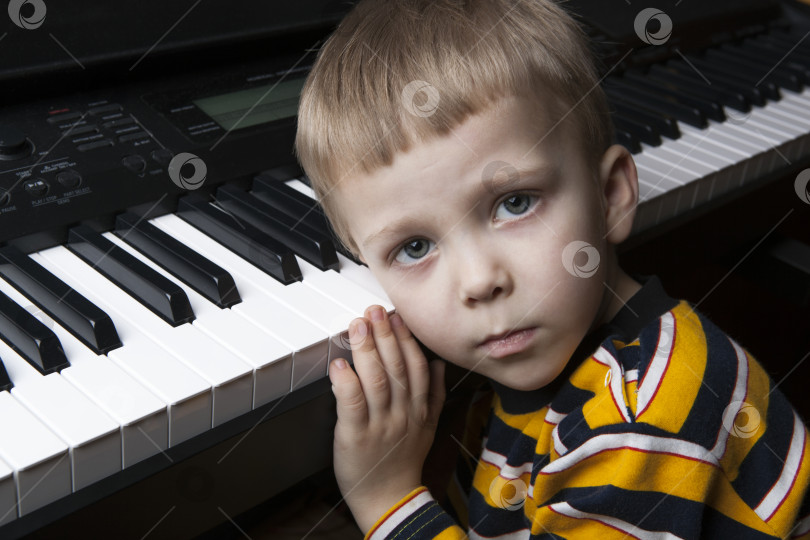 Скачать мечтающий маленький мальчик, сидящий за пианино фотосток Ozero