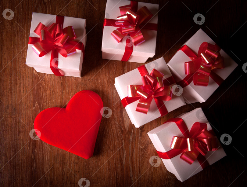 Скачать белые праздничные подарочные коробки с красными бантами на деревянном столе с красным сердцем фотосток Ozero