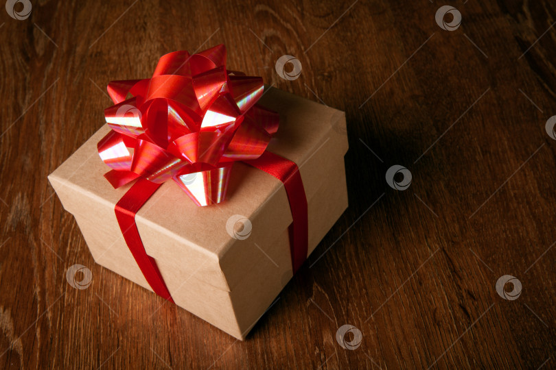 Скачать Одна праздничная подарочная коробка с красным бантом на деревянном столе фотосток Ozero
