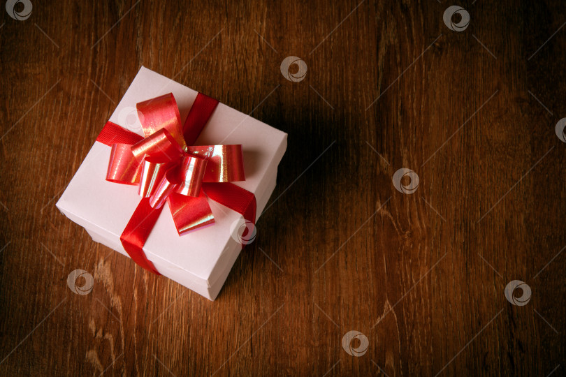 Скачать Одна белая праздничная подарочная коробка с красным бантом на деревянном столе фотосток Ozero