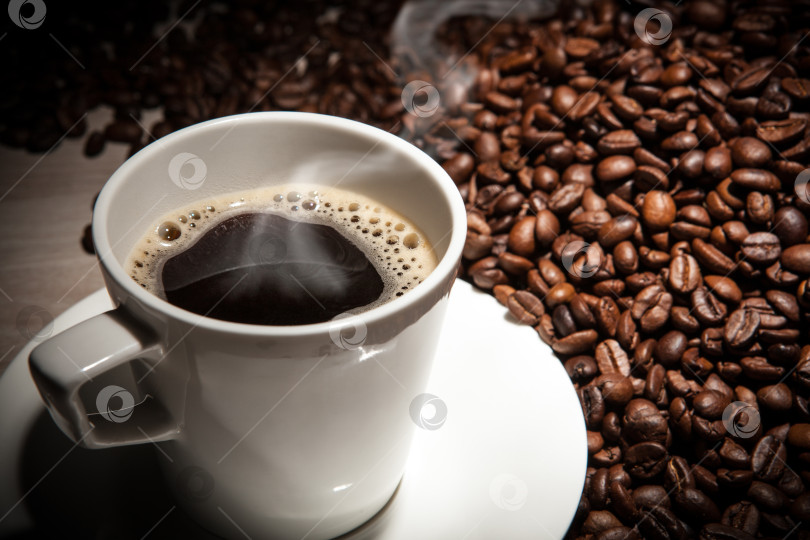 Скачать белая чашка кофе с паром на фоне обжаренных кофейных зерен фотосток Ozero