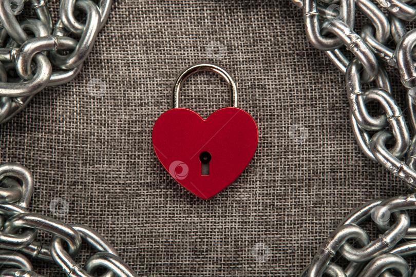 Скачать красный навесной замок в форме сердца со стальной цепочкой на сером льняном текстиле фотосток Ozero