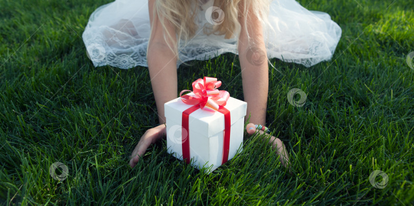 Скачать маленькая девочка в белом платье с подарочной коробкой на зеленой лужайке фотосток Ozero