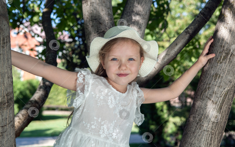 Скачать маленькая девочка в белом платье и панамке сидит на дереве фотосток Ozero