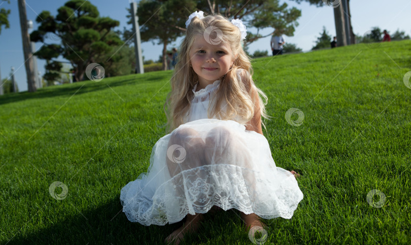 Скачать маленькая девочка с распущенными волосами в белом платье сидит на зеленой траве фотосток Ozero
