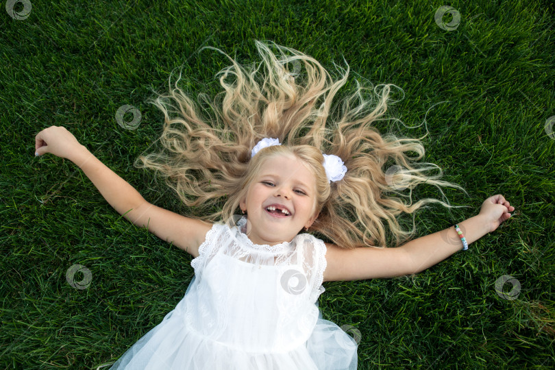 Скачать маленькая девочка с распущенными волосами в белом платье лежит на зеленой траве фотосток Ozero