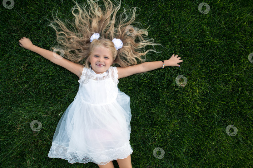 Скачать маленькая девочка с распущенными волосами в белом платье лежит на зеленой траве фотосток Ozero
