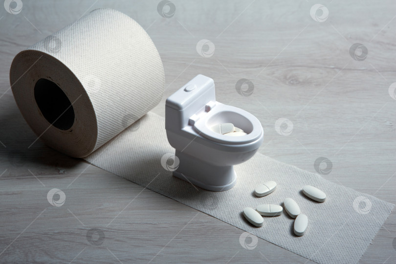 Скачать миниатюрный унитаз и таблетки с рулоном туалетной бумаги на столе фотосток Ozero