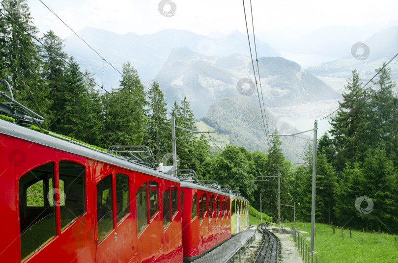 Скачать Красный панорамный поезд на фоне Альп и горных озер. Крутой подъем по рельсам на вершину горы Пилатус. Швейцария, Европа фотосток Ozero
