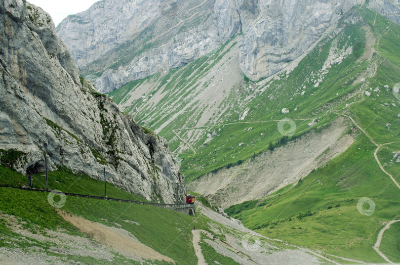 Скачать Красный поезд вдалеке движется по железной дороге в горах Швейцарии. Поднимитесь по неровной дороге на вершину Пилатуса. фотосток Ozero