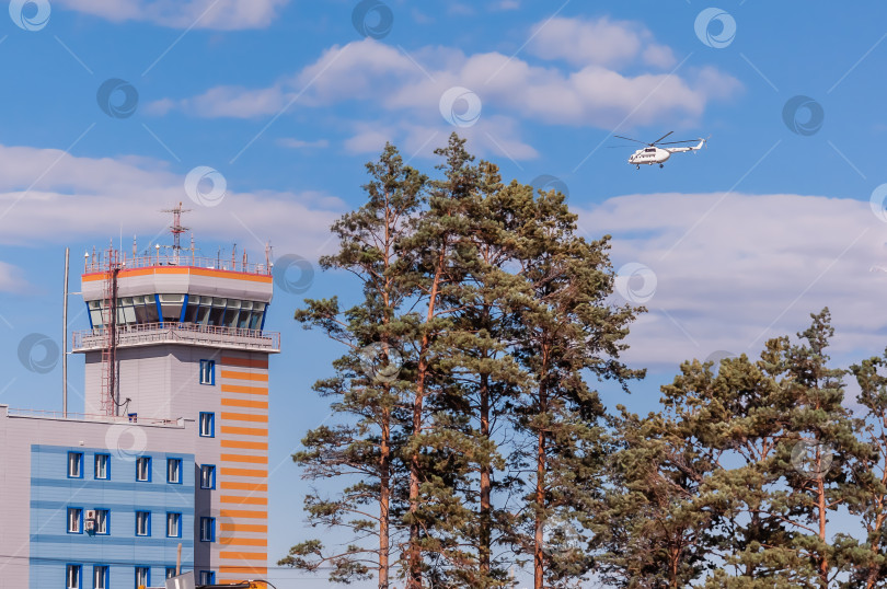 Скачать Белый вертолет летит рядом с вышкой управления полетами на фоне голубого неба с облаками. фотосток Ozero