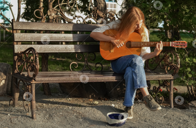 Скачать Счастливая девушка играет на гитаре на скамейке в парке. Прогулка на свежем воздухе. Студент изучает музыку. Хобби для подростка. фотосток Ozero