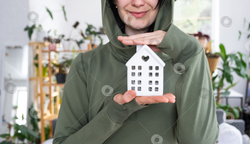Скачать Счастливая женщина в своем доме держит в руках миниатюрную фигурку дома и ключ в интерьере. Проект дома мечты, покупка недвижимости, страхование, ипотека, аренда, бронирование фотосток Ozero