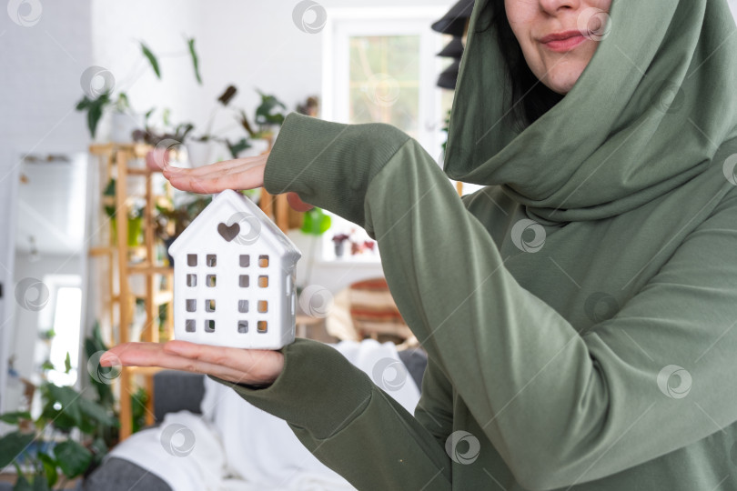Скачать Счастливая женщина в своем доме держит в руках миниатюрную фигурку дома и ключ в интерьере. Проект дома мечты, покупка недвижимости, страхование, ипотека, аренда, бронирование фотосток Ozero