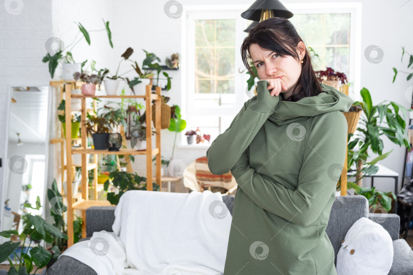 Скачать Вдумчивые эмоции женщины в ее доме в ярком современном интерьере с домашними растениями. Портрет мечтательной фотосток Ozero
