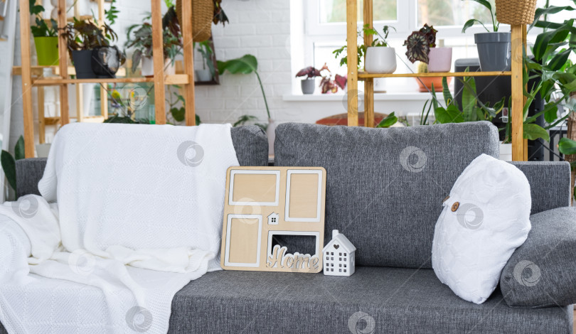 Скачать Ключ от дома с брелком и макетом миниатюрного дома в рамке на сером диване в белом интерьере с растениями в горшках. Дизайн, проект, переезд в новый дом, ипотека, аренда и покупка недвижимости фотосток Ozero