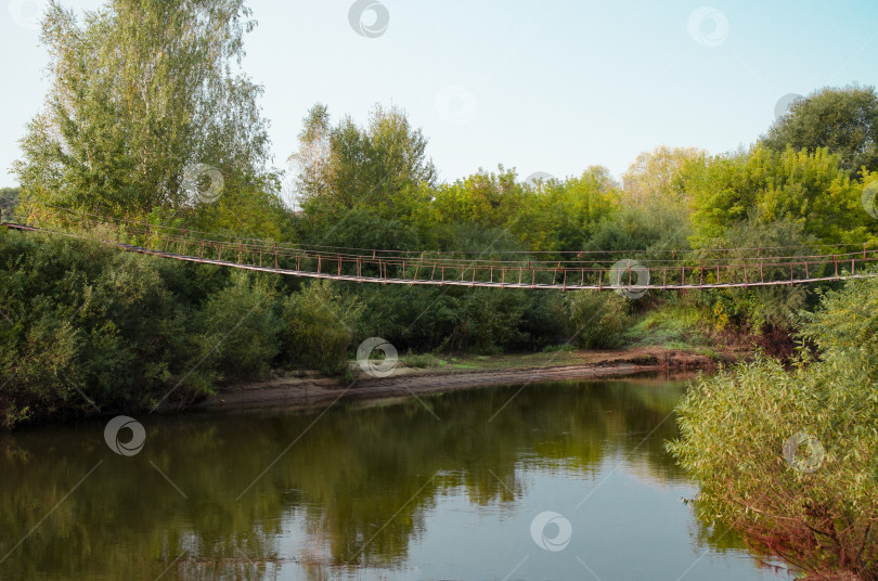 Скачать Вид на старый деревянный подвесной мост через реку в дикой местности. Прекрасный летний пейзаж. фотосток Ozero