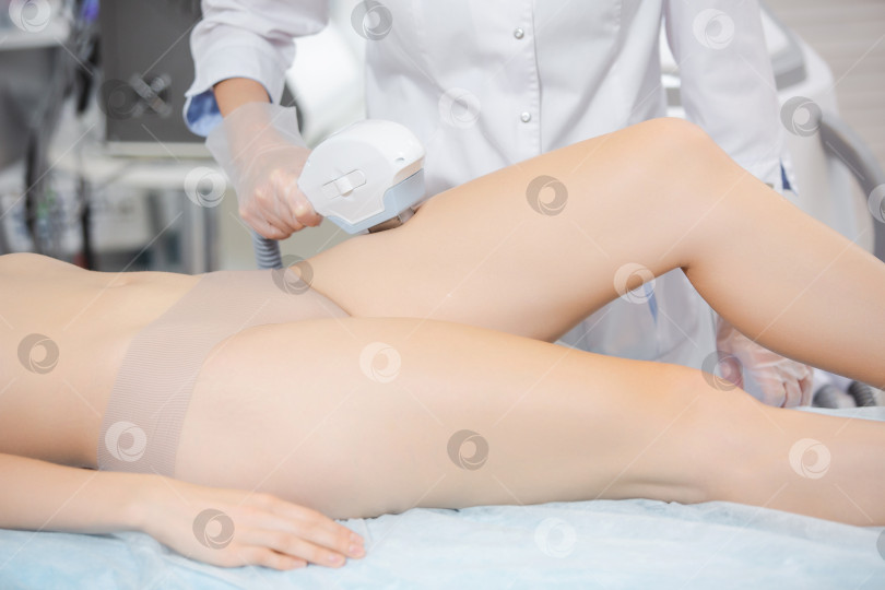 Скачать Фотография симпатичной женщины-врача в специальных защитных очках, которая проводит процедуру лазерной эпиляции, удаление волос на ногах современными методами фотосток Ozero