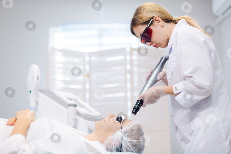 Скачать Снимок лица молодой девушки в защитных очках с видом сбоку во время процедуры карбонового пилинга в салоне красоты фотосток Ozero