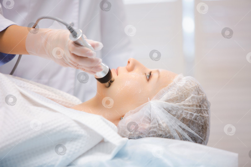 Скачать Крупным планом портрет красивой улыбающейся женщины, отдыхающей во время процедуры RF-лифтинга в современном салоне красоты фотосток Ozero
