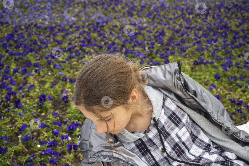 Скачать Девочка-подросток на лужайке с фиолетовыми цветами в парке. Девушка и весенний цветок. Открытый романтический портрет молодой счастливой и привлекательной девушки в клетчатой толстовке с капюшоном, наслаждающейся беззаботным времяпрепровождением фотосток Ozero